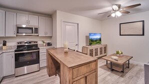 Une cuisine avec des meubles blancs, un four à micro-ondes, une cuisinière et un ventilateur de plafond.