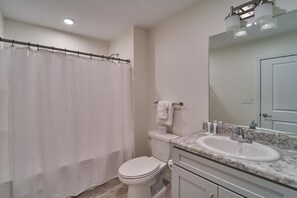 A bathroom with a shower curtain, toilet, sink, mirror, and towel rack. - The Ruby 307 (Pigeon Forge)