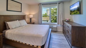 Quarto com cama de madeira, mesa de cabeceira, penteadeira, janela com cortinas e um quadro na parede.