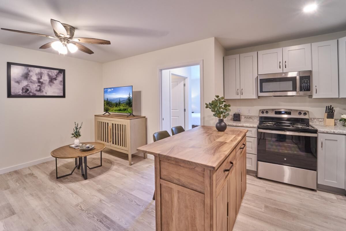 A modern kitchen with white cabinets, a microwave, a stove, and a dining area with a table and chairs.