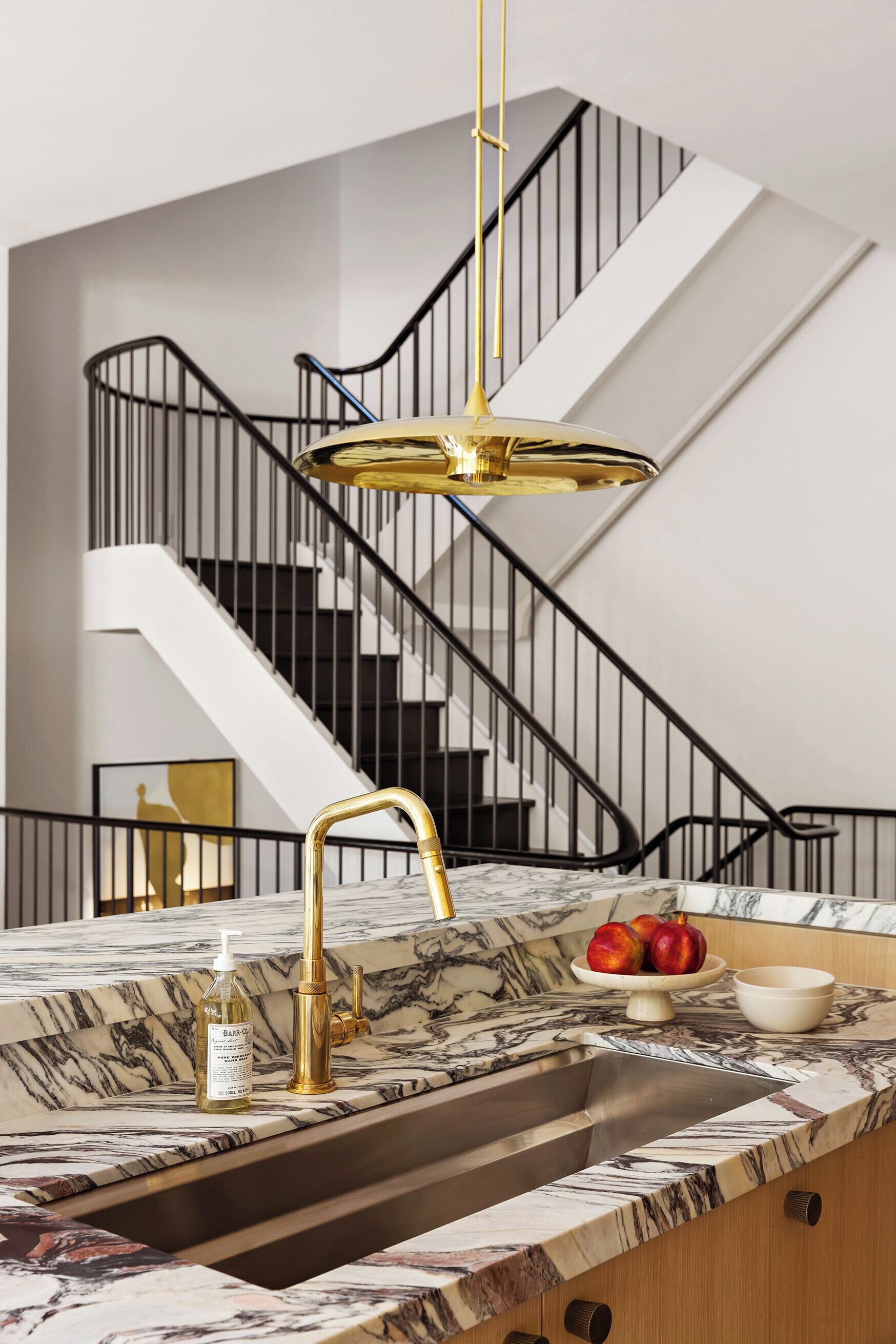 Une cuisine moderne dotée d’un plan de travail en marbre, d’un robinet doré et offrant une vue sur un escalier.