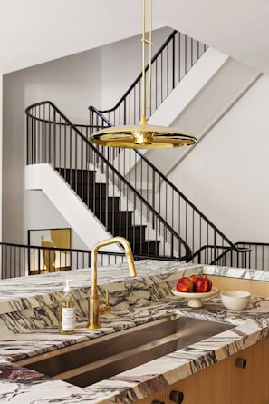 A modern kitchen with a marble countertop, gold faucet, and a view of a staircase.
