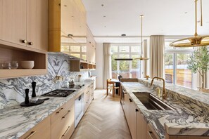 A modern kitchen with marble countertops, wooden cabinets, and a large window.
