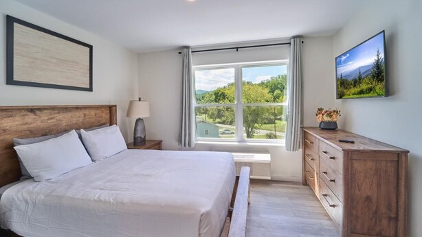 A bedroom with a bed, a nightstand, a dresser, a window with a view, and a framed picture on the wall. - The Ruby 308 (Pigeon Forge)