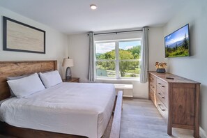 Un dormitorio con cama, mesita de noche, cómoda, ventana con vistas y un cuadro en la pared.