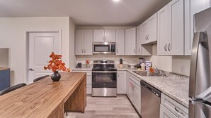 A modern kitchen with white cabinets, stainless steel appliances, and a wooden dining table. - The Ruby 308 (Pigeon Forge)