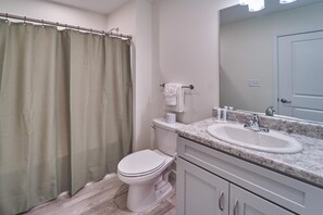 A bathroom with a shower curtain, toilet, sink, and mirror. - The Ruby 308 (Pigeon Forge)