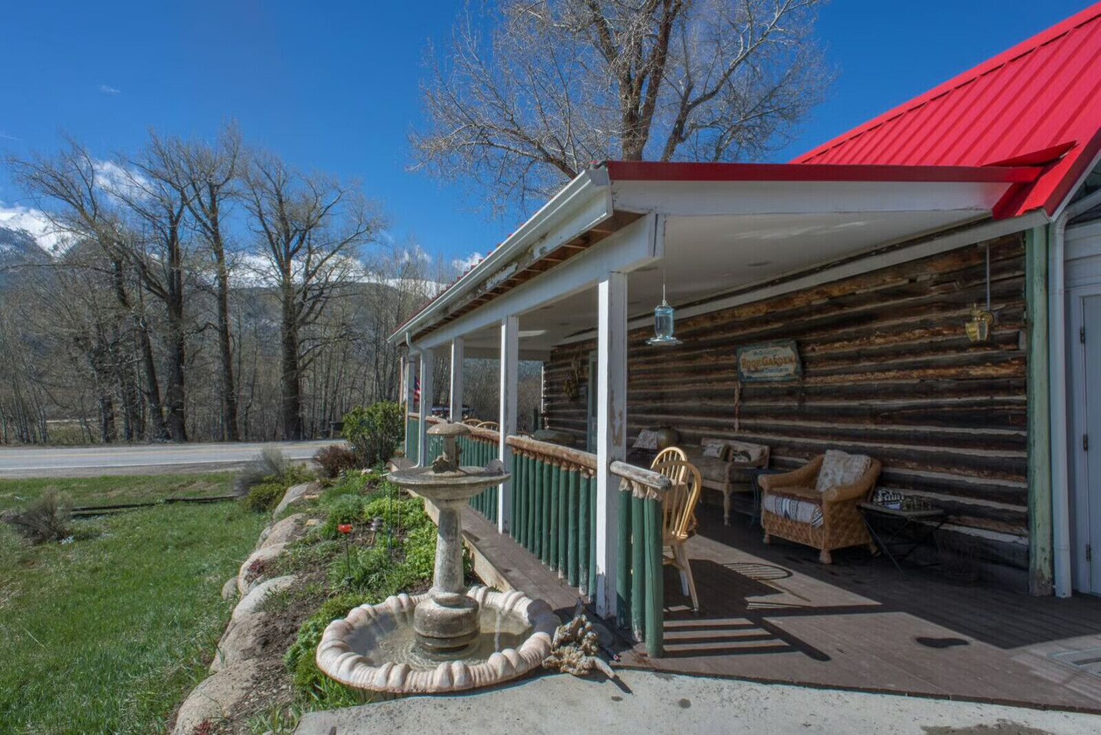 Une cabane rustique en rondins de bois, dotée d’un porche, d’une fontaine en pierre et d’une chaise.