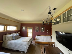 Un dormitorio con dos camas, televisión, mesa de comedor y candelabro.