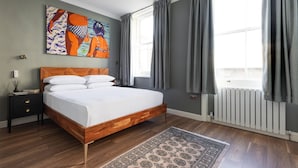 Une chambre à coucher avec un lit en bois, une table de chevet, un ventilateur de plafond, un radiateur et une grande fenêtre avec des rideaux.