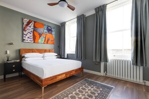 Ein Schlafzimmer mit einem hölzernen Bett, einem Nachttisch, einem Deckenventilator, einer Heizung und einem großen Fenster mit Vorhängen.
