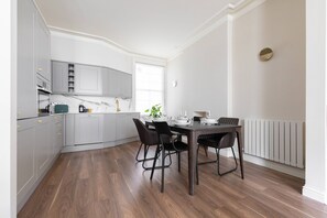 A modern kitchen with grey cabinets, a dining table with chairs, and a window providing natural light. - Abingdon Road IV - Two Bedroom Apartment, Sleeps 4 (London)