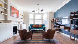 Un salon comprenant un canapé, deux fauteuils, une table basse, un tapis à motifs, une bibliothèque et une cheminée.