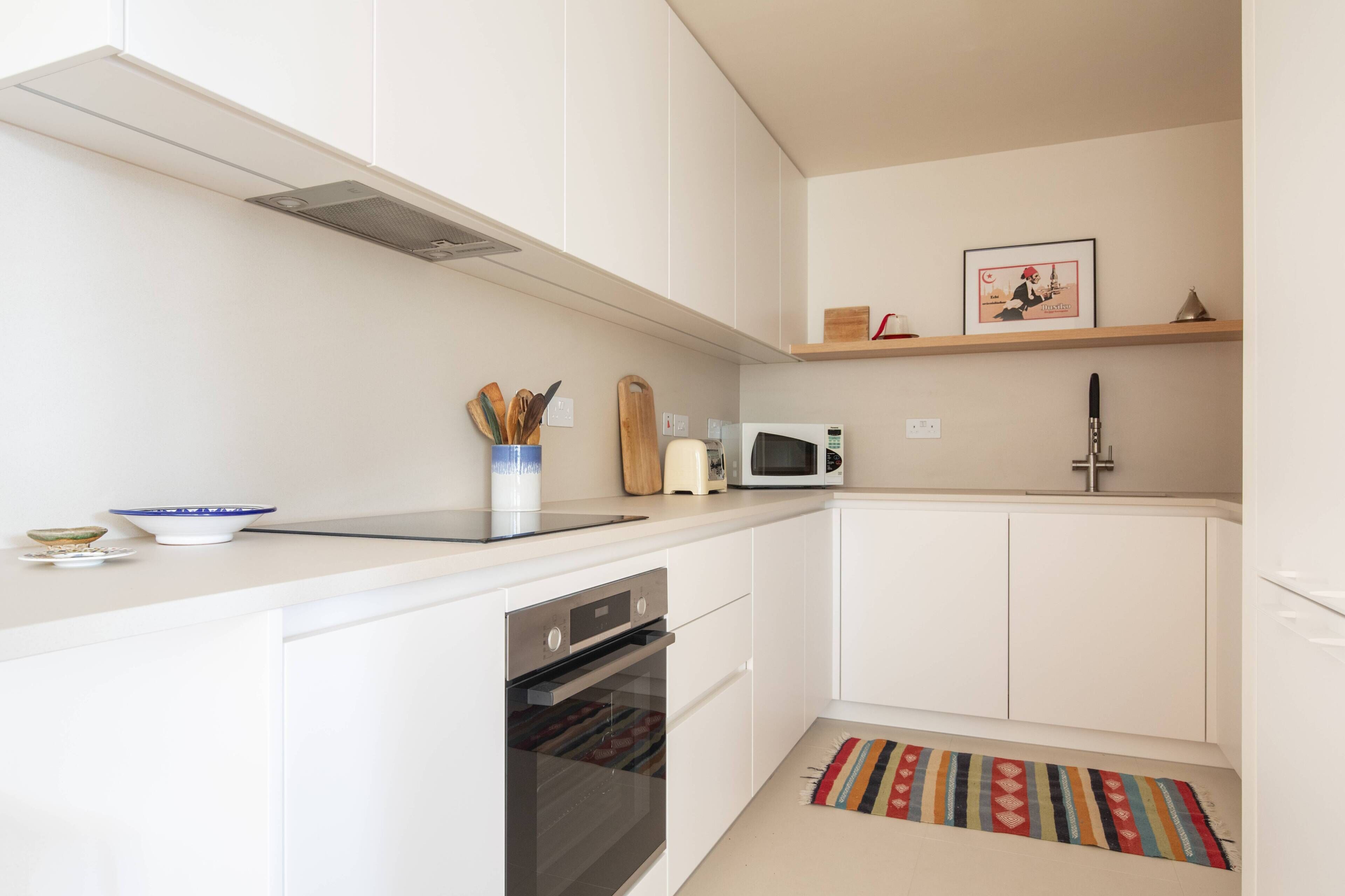 A modern kitchen with white cabinets, a microwave, a sink, and a stove.