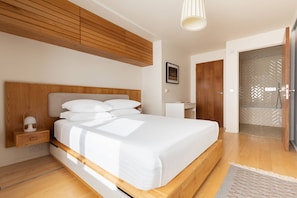 A modern bedroom with a wooden headboard, a bedside table with a lamp, a large bed with white bedding, and a walk-in closet with a patterned door. - Hardwick Street III - Two Bedroom Apartment, Sleeps 4 (London)