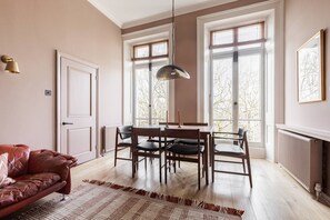 Ein Zimmer mit Esstisch, Stühlen, einer Couch und großen Fenstern.