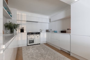 Eine moderne Küche mit weißen Schränken, einem eingebauten Backofen und einer großen Kochinsel mit Marmorarbeitsplatte.