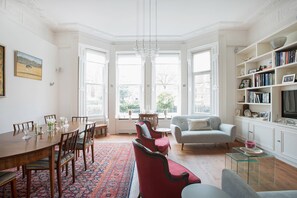 Ein geräumiges Zimmer mit Esstisch, Stühlen, einer Couch, einem Bücherregal und einem Fernseher.