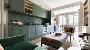 Ein geräumiger Wohnbereich mit einem grünen Sofa, einem gemusterten Hocker und einem Essbereich mit einer roten Lampe.