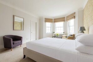Ein Schlafzimmer mit einem großen Bett, einem Sessel, einem Schreibtisch und einem Fenster mit Vorhängen.