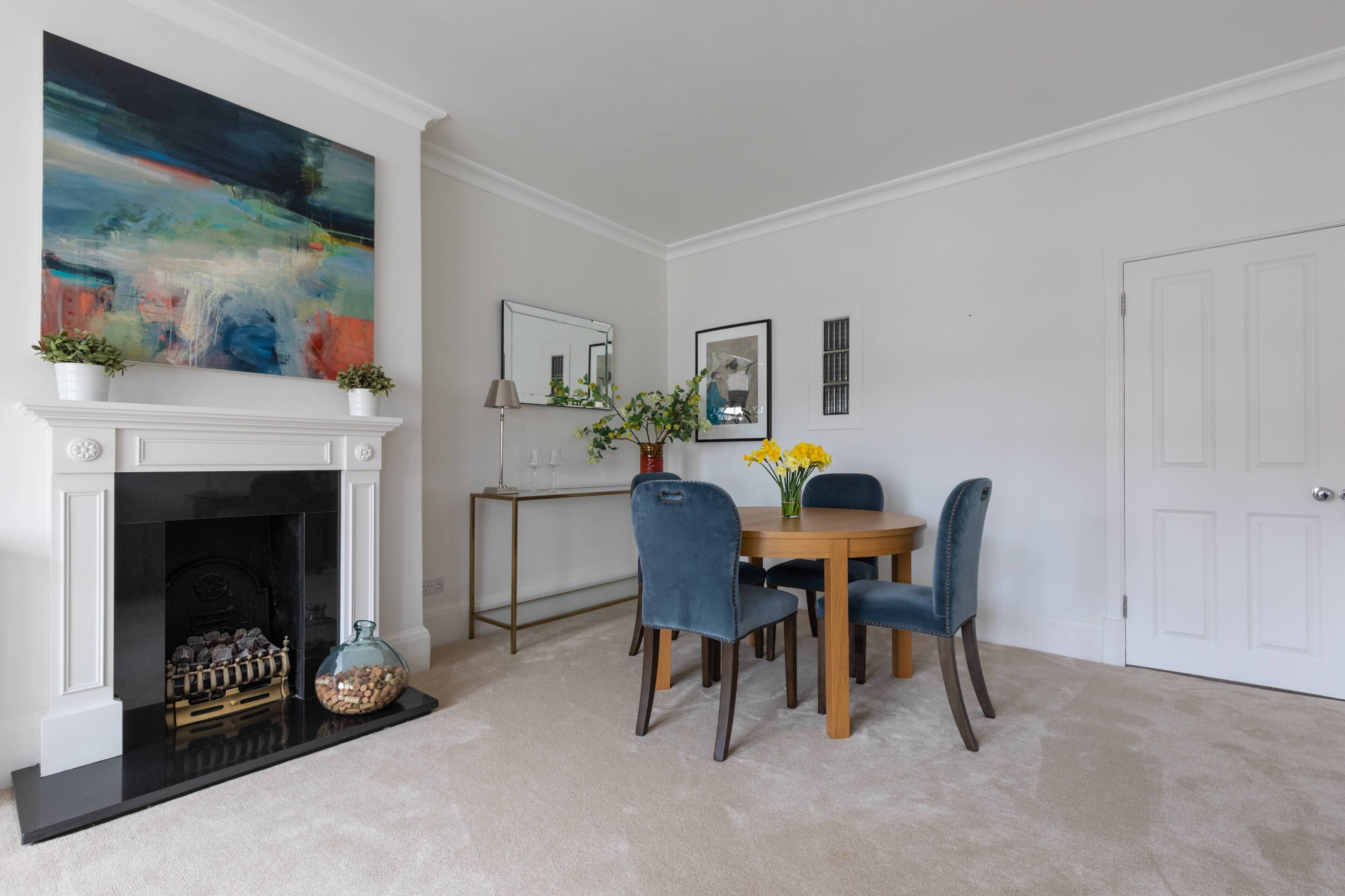 A dining room with a fireplace, a table with chairs, and a large abstract painting on the wall.