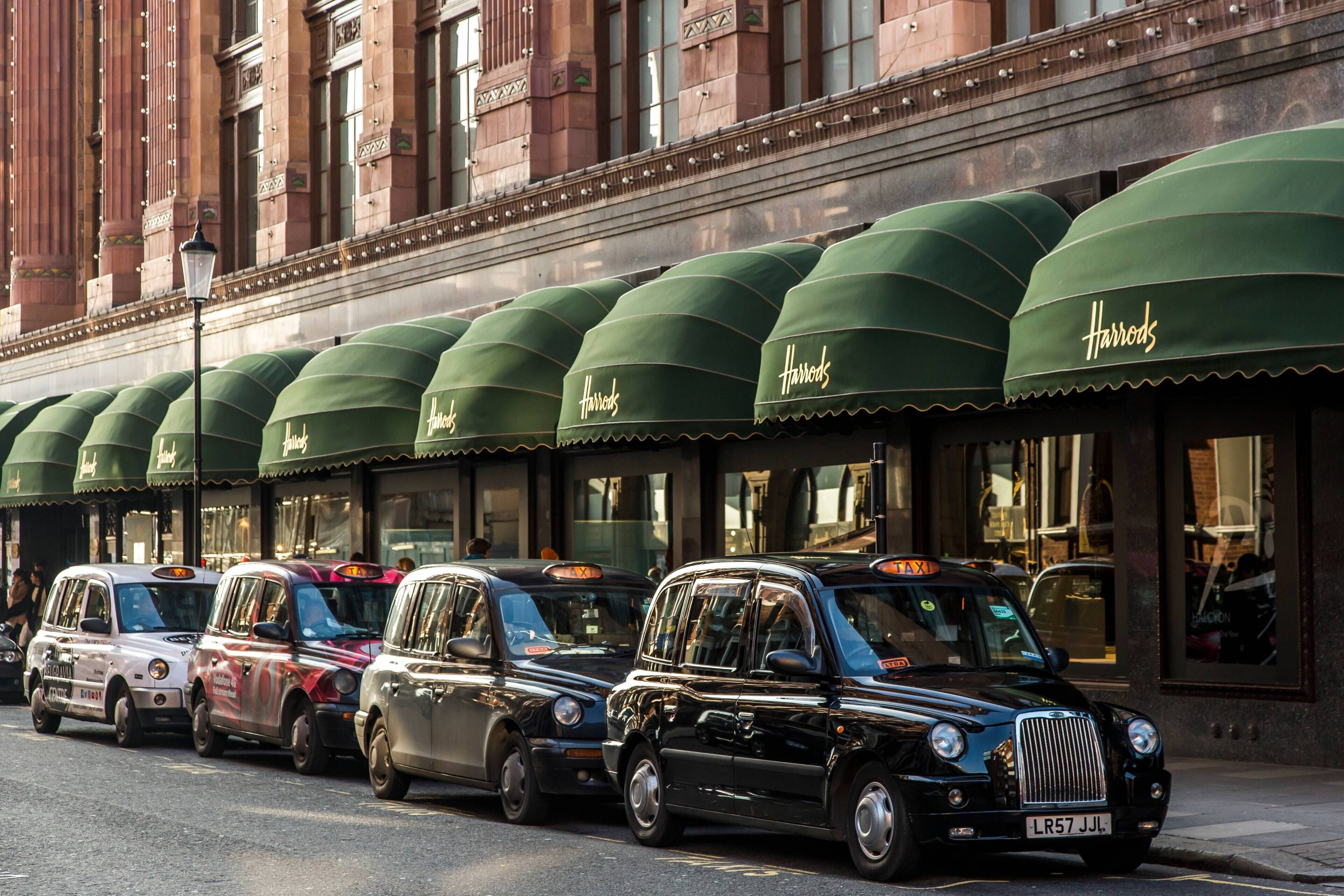 A row of taxis parked in front of a building with green awnings labeled 'Harrods.'