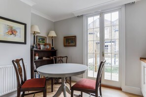 A dining area with a round table, chairs, a bookshelf, and a large window with a view of buildings. - First Street II - Two Bedroom Apartment, Sleeps 4 (London)