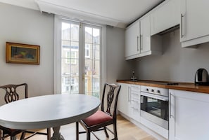 A kitchen with white cabinets, a wooden countertop, a round dining table, and a red cushioned chair. - First Street II - Two Bedroom Apartment, Sleeps 4 (London)