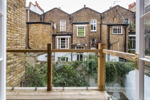 A view from a balcony with a wooden railing, overlooking a row of brick houses with visible windows and a brick wall. - First Street II - Two Bedroom Apartment, Sleeps 4 (London)
