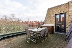 Eine Dachterrasse mit Tisch und Stühlen, einer Ziegelwand und einer Tür.