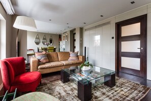 Ein modernes Wohnzimmer mit einem Glastisch, einem roten Sessel, einem beigen Sofa und einem gemusterten Teppich.