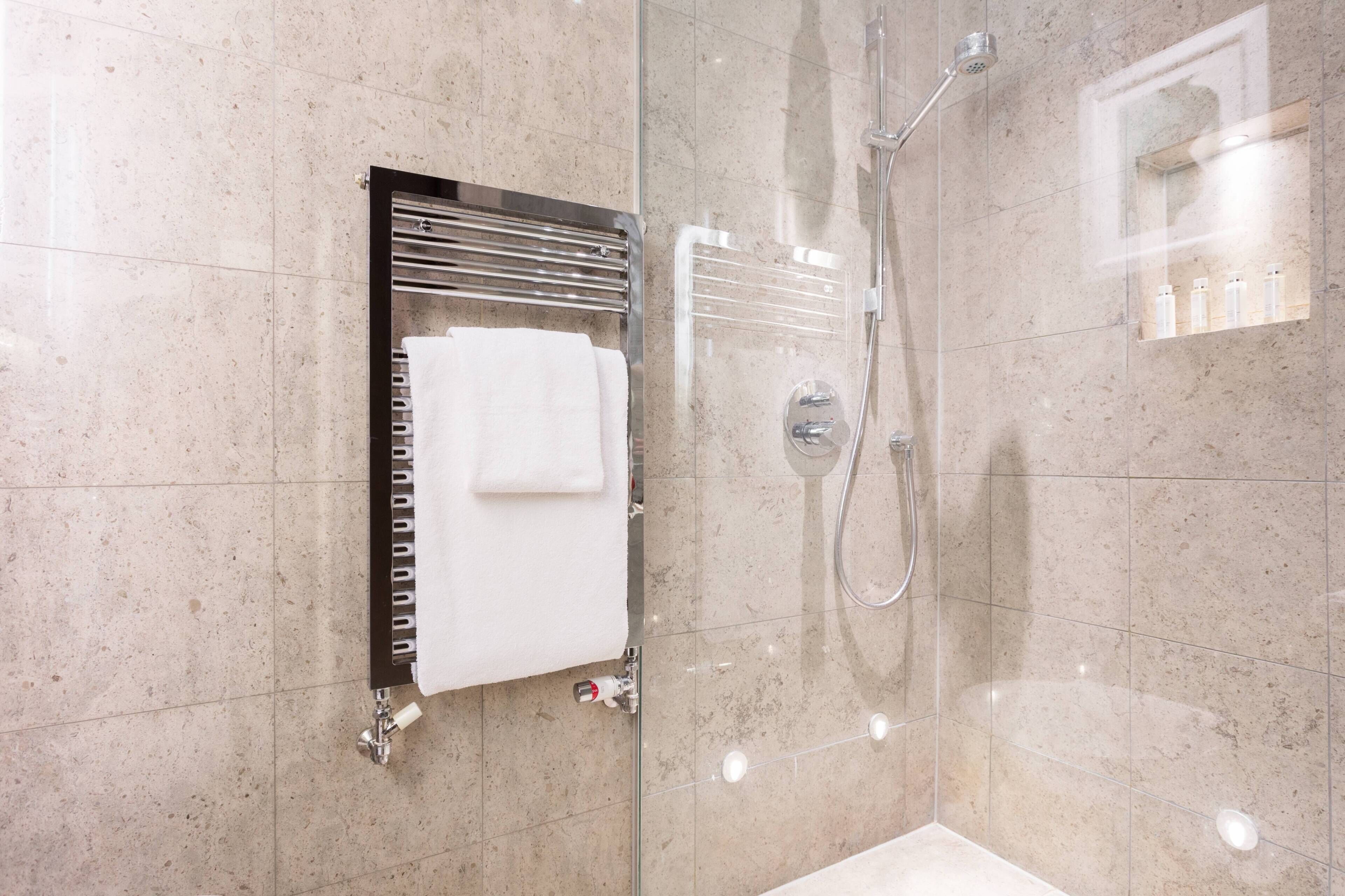 Un bagno moderno con doccia a vetro, un portascopevoli con un asciugamano bianco e uno specchio con ripiano per articoli da toilette.