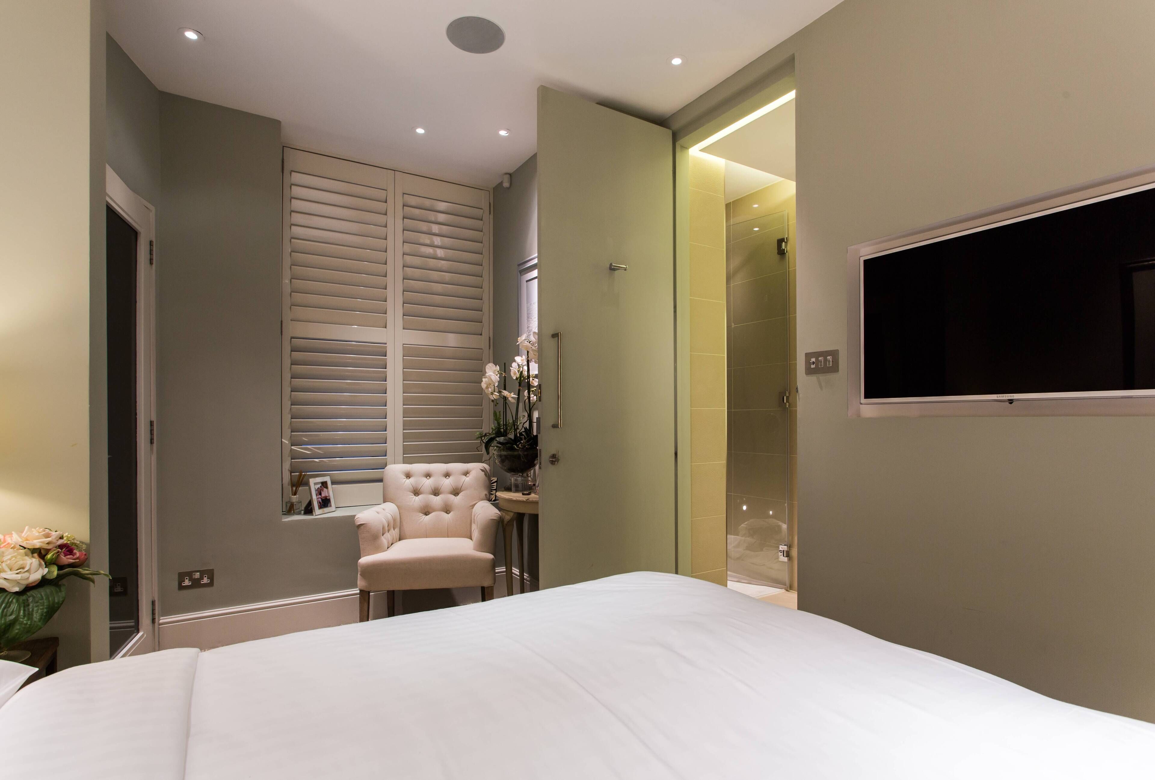 A bedroom with a bed, a chair, a vanity, and a shower area.
