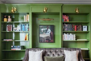 Ein grüner Raum mit einer раppelten Couch und Bücherregalen, gefüllt mit Büchern und dekorativen Gegenständen.