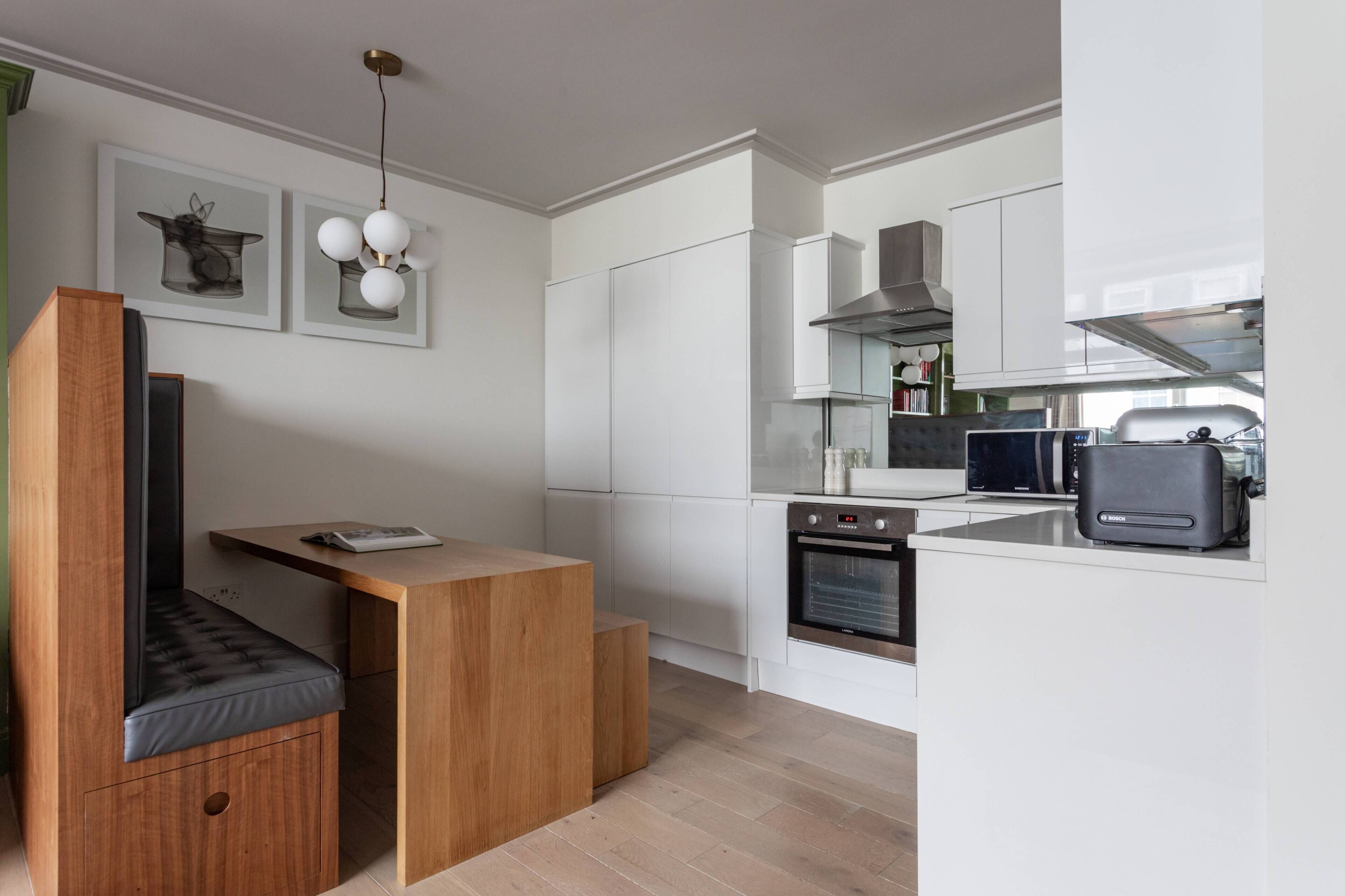 Eine moderne Küche mit weißen Schränken, einem eingebauten Backofen, einem Toaster und einer hölzernen Sitzbank mit Polsterung.