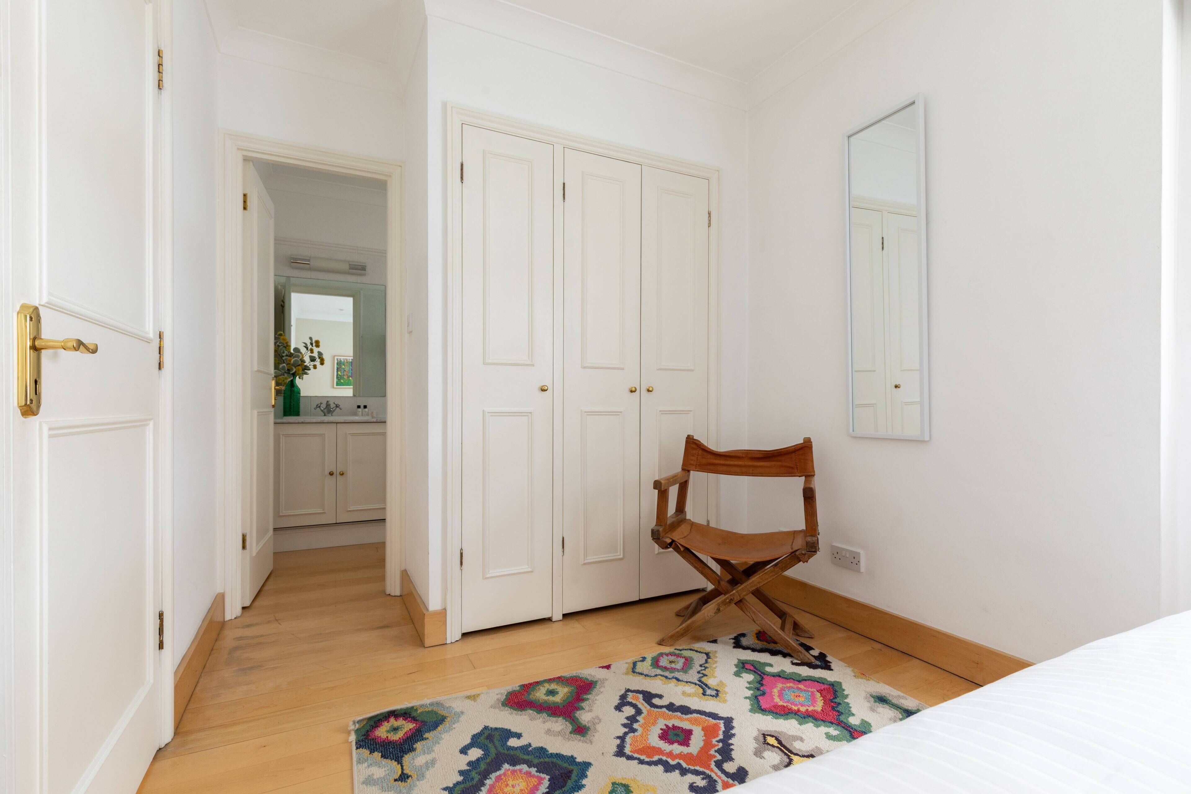 Um quarto com uma cama, uma cadeira de madeira, um tapete estampado e um guarda-roupa branco.