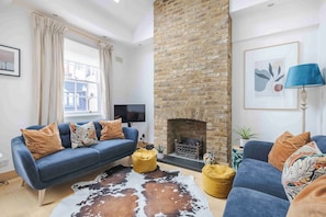 A living room with a blue sofa, a fireplace, a television, and a cowhide rug. - Bathurst Mews III - Two Bedroom Apartment, Sleeps 4 (London)