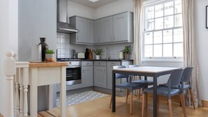 Une cuisine moderne avec des meubles de couleur grise, une table à manger avec des chaises, une fenêtre avec des rideaux et une petite plante en pot posée sur le comptoir.