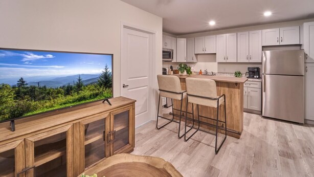 A modern kitchen with a large TV, wooden bar stools, and a stainless steel refrigerator. - The Ruby 311 (Pigeon Forge)
