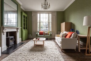 Ein Wohnzimmer mit Kamin, grünen Schränken, einer Couch, einem Couchtisch und einer Chandelüster.