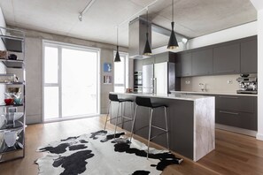 Eine moderne Küche mit Kochinsel, Barhocker, Pendelleuchten und einem Kuhfellteppich.