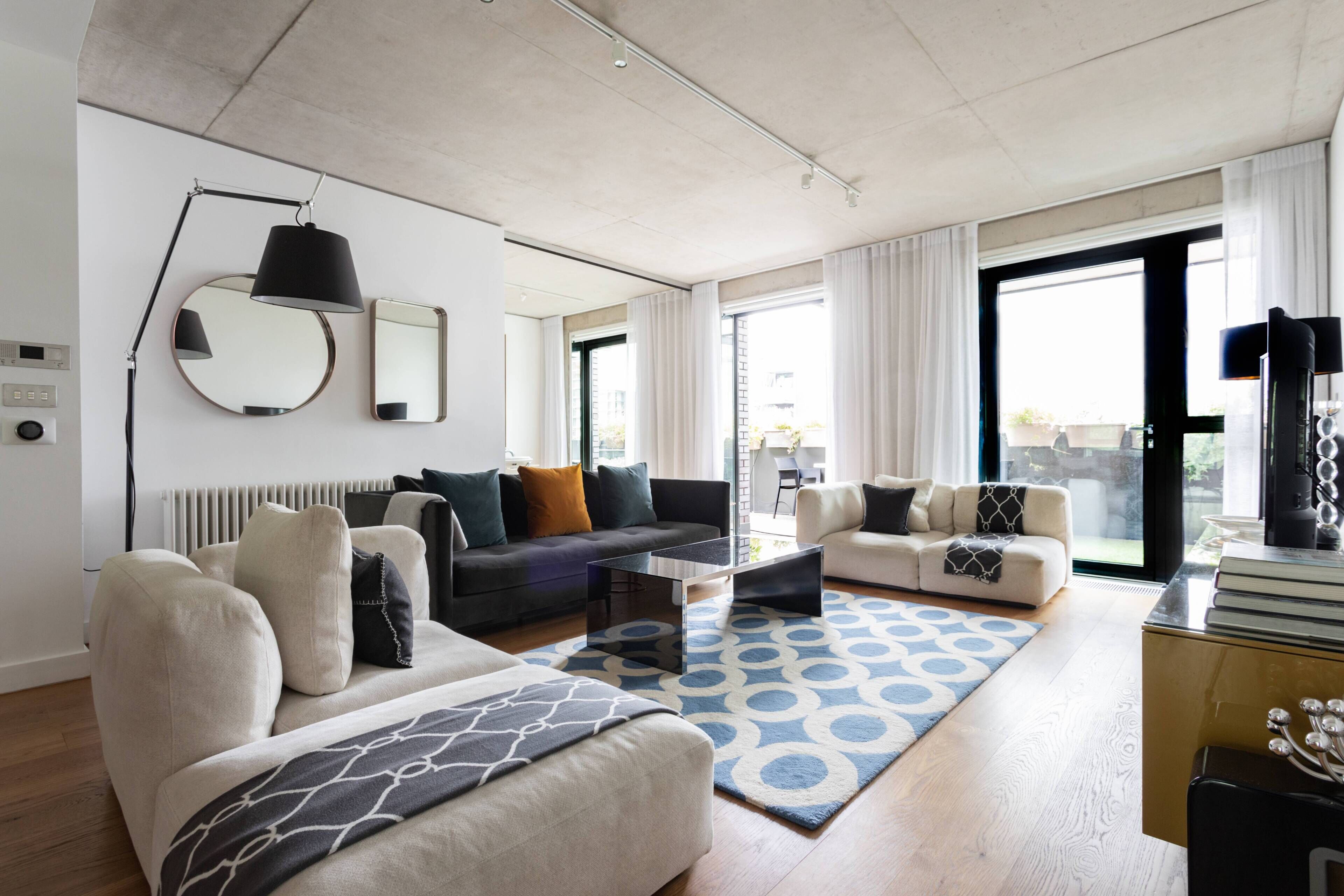 A modern living room with a sofa, armchair, coffee table, and a patterned rug.