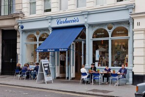 Ein Café mit Außenbestuhlung, einer blauen Markise und einem Schild mit der Aufschrift 'Carluccio's'.