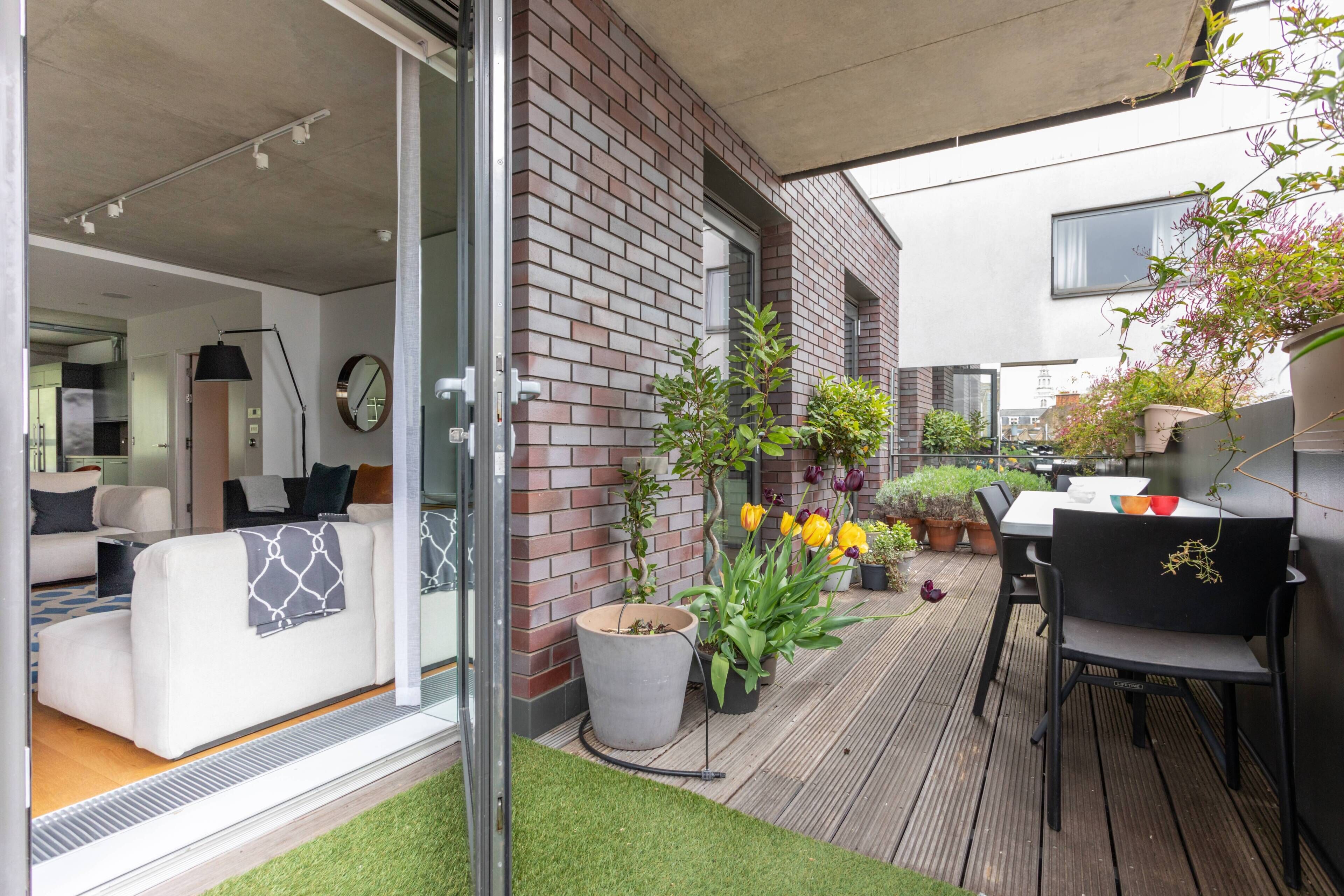 Eine moderne Terrasse mit Ziegelmauer, Pflanzgefäßen und Gartenmöbeln.