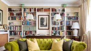 A green sofa, a glass coffee table with books, and a bookshelf filled with books and lamps. - Courtfield Mews - Four Bedroom House, Sleeps 8 (London)