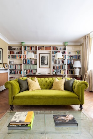 A green sofa, a glass coffee table with books, and a bookshelf filled with books and lamps. - Courtfield Mews - Four Bedroom House, Sleeps 8 (London)