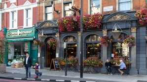 A building with a green sign for 'OPATRA RESTAURANT' and 'SMITH'S ALE & PINTS' with flower baskets above the windows. - Gertrude Street III - Two Bedroom Apartment, Sleeps 4 (London)