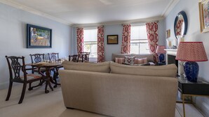 A living room with a beige sofa, wooden dining table, chairs, patterned curtains, and a vase on a side table. - Gertrude Street III - Two Bedroom Apartment, Sleeps 4 (London)