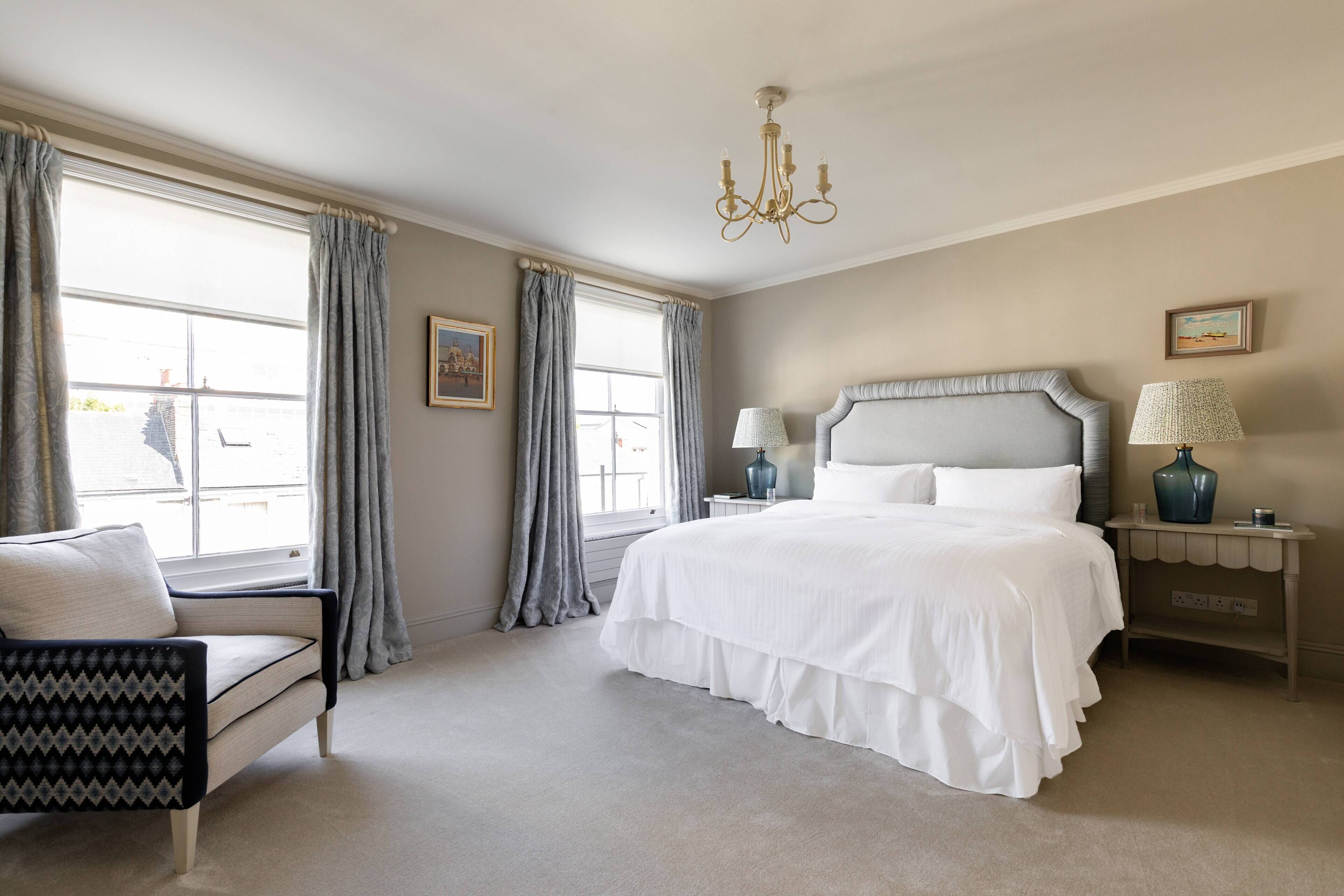 A bedroom with a bed, a chair, a nightstand, a lamp, and a chandelier.