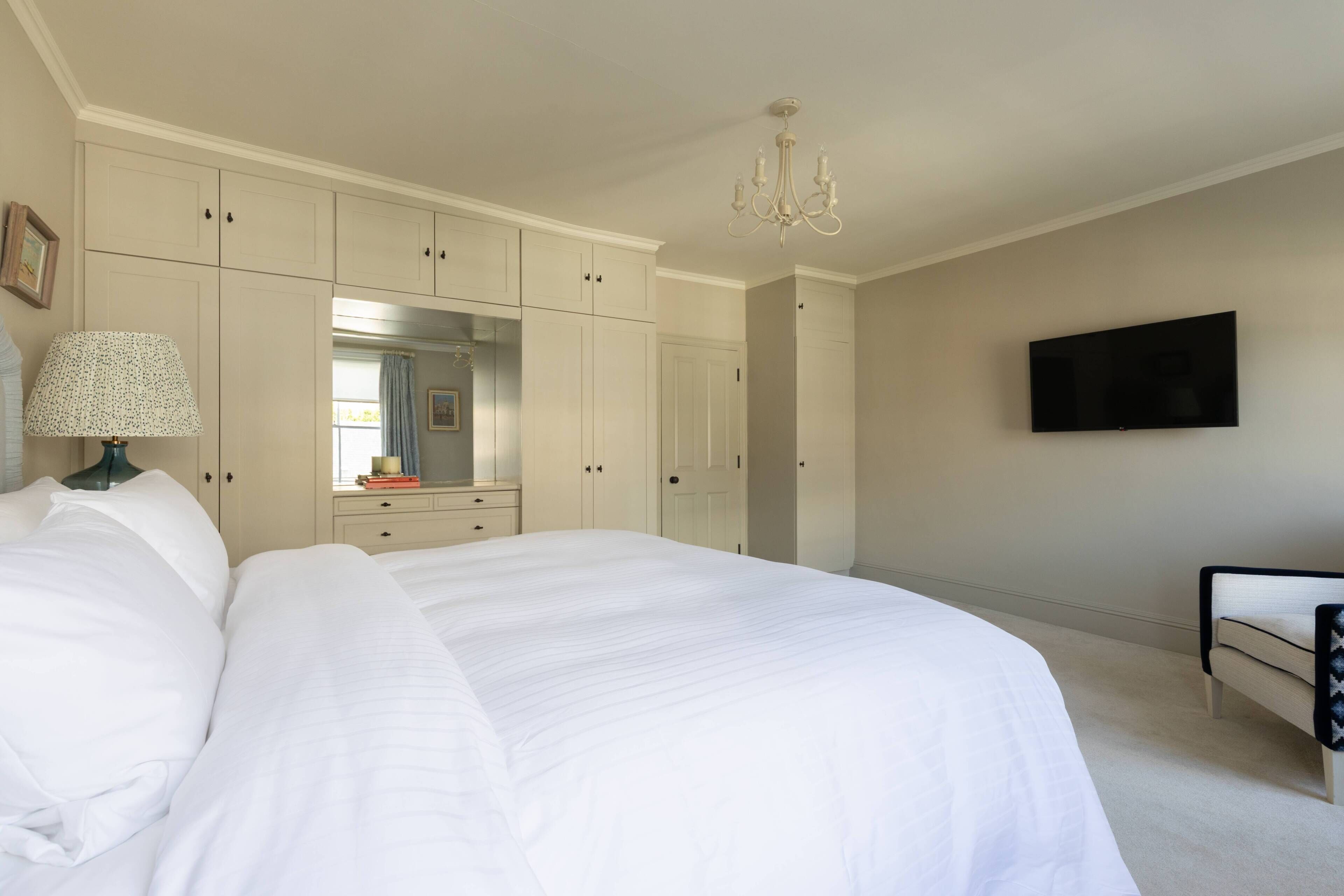 A bedroom with a large bed, a dresser, a mirror, a television, and a chandelier.